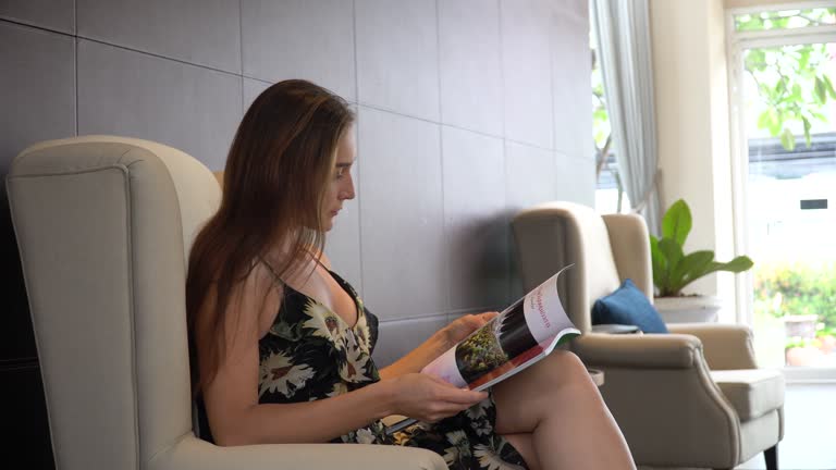 woman waiting in lobby sitting on sofa and reading magazine at hotel