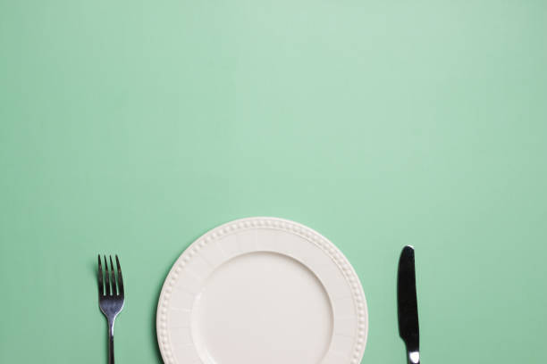 istock A white plate with fork and knife on green background with copy space. 1496041679