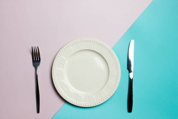 istock A white plate with fork and knife on pink and blue background. 1496041691