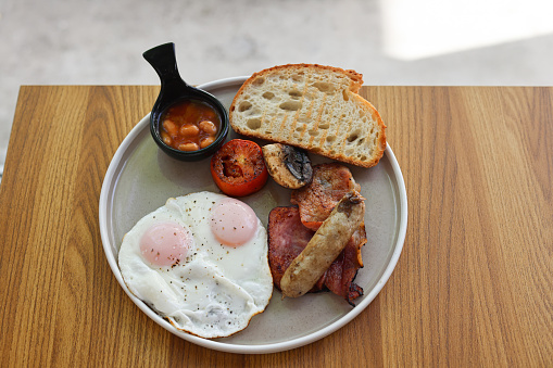 English breakfast with fried egg, sausage, bacon, beans and toast on white background copy space