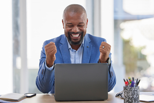 Happy black man, laptop and celebration for winning, sale or good news on discount at the office desk. Excited African American male celebrating on computer for promotion, bonus or achievement