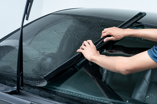 Male auto specialist worker hand rolling car window film on front windscreen glass surface. Car side window film removal and tinting installation.