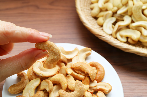 Person Picking a Roasted Cashew Nut Kernel from Snack Saucer