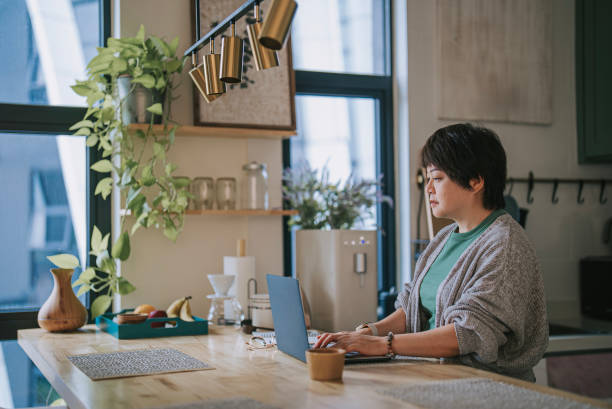istock Asian mature chinese woman working at home at kitchen counter using laptop 1496048673