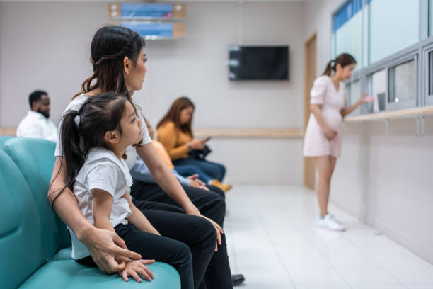 Asian family patient wait on line queue to receive medicine in hospital. Attractive mother and daughter sit on chairs, waiting the pharmacy counter to provides services to patients in medical center. paciente familiar asiático espera en la cola para recibir medicamentos en el hospital. la atractiva madre y su hija se sientan en sillas, esperando en el mostrador de la farmacia para brindar servicios a los pacientes en el centro médico.