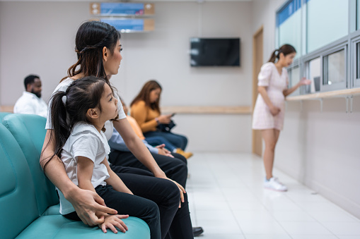 Asian family patient wait on line queue to receive medicine in hospital. Attractive mother and daughter sit on chairs, waiting the pharmacy counter to provides services to patients in medical center.