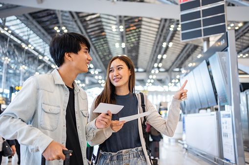 Asian young couple passenger walk in airport terminal to boarding gate. Attractive beautiful female tourist friends feeling happy and excited to go travel abroad by airplane for holiday vacation trip.