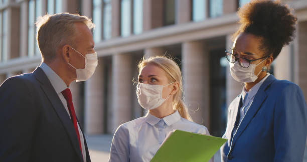 istock Mixed-races office employees in protective mask discussing contract outdoors downtown 1496053952