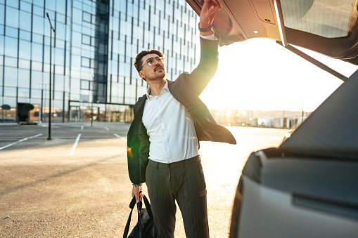 Successful businessman taking luggage from the car trunk outdoors