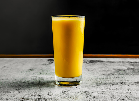 mango lassi or milk shake with yogurt, sugar, water and ice served in glass side view on grey background drink