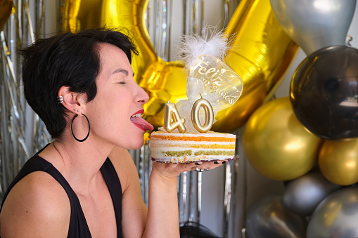 Caucasian woman in her 40 birthday party with a cake with candles, sticking out the tongue.