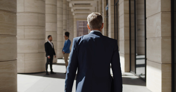 Back view of confident businessman walking outside office. Mature entrepreneur in suit with briefcase commuting to work outdoors modern business center