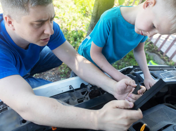 Shock due to irreparable damage. Timing belt break. Man and son near hood of car is looking for a malfunction due to which the engine does not work. Driver is holding a broken front belt in his hands. rotura de la correa de distribución. el hombre y el hijo cerca del capó del automóvil están buscando un mal funcionamiento debido a que el motor no funciona. el conductor sostiene un cinturón delantero roto en sus manos. choque debido a daños irrepar