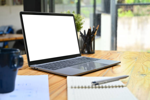 istock Wooden office desk with laptop computer, notepad, and cup of coffee. White blank screen for your advertising text. 1496059464