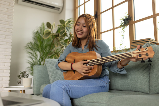 Young Burmese woman playing a ukulele in the living room of her home