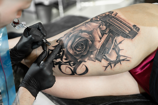 Close up image of the bearded tattoo male artist makes a tattoo on a female leg