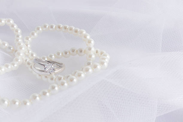 istock Beautiful wedding background for design. Two white gold engagement rings with a diamond on a white delicate bridal veil with pearl beads. 1496064886