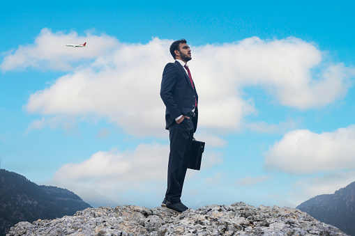 Young businessmen standing on top mountain and airplane flying over mountains.