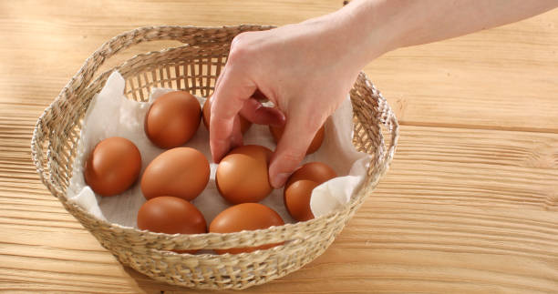 istock Man puts raw Eggs in a basket on a wooden background. Close-up. High angle view. 1496067174
