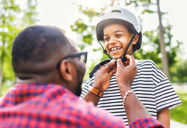 istock Happy family: father puts on  son helmet for safe cycling in park 1496067512