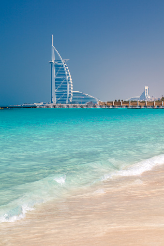 Dubai, UAE  april 06, 2023: Sufouh Beach turquoise transparent water in sea, surf, sand, Burj Al Arab, vertical frame, waves rolling in sand