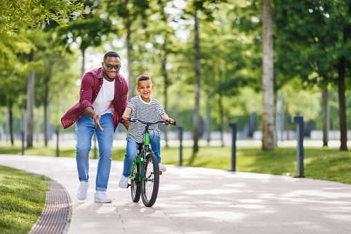 Happy african american family  father teaches boy son  to ride bike in  park   in nature