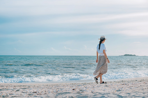 Rear view of beautiful young woman with summer hat walking on the sandy beach