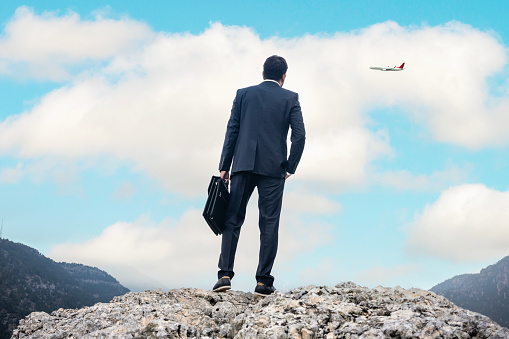 Young businessmen standing on top mountain and airplane flying over mountains.