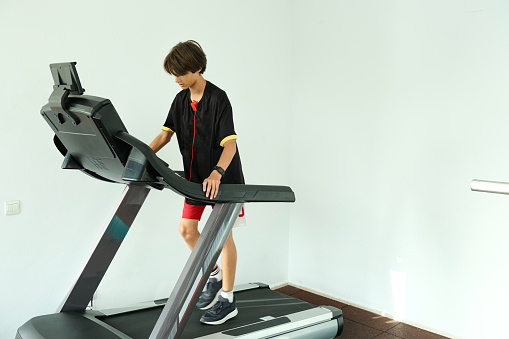 Teenage boy running on treadmill in gym. Sport, cardio, strength training, fitness concept.