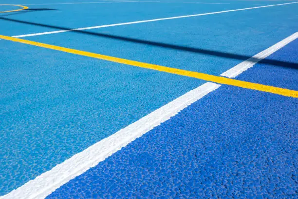 Photo of Sport field court background. Blue rubberized and granulated ground surface with white, yellow lines on ground. Top view