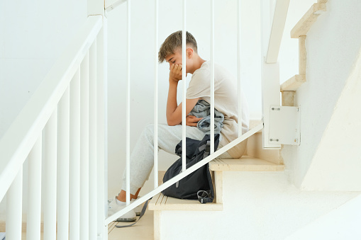 Sad frustrated teenage boy with backpack sitting on stairs alone. Education difficulties, problem with family, emotion, anxiety, depression in adolescence concept.