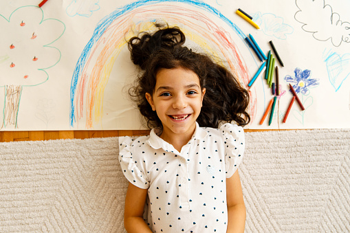 Above shot of smiling little girl posing with her crayon drawing on the floor