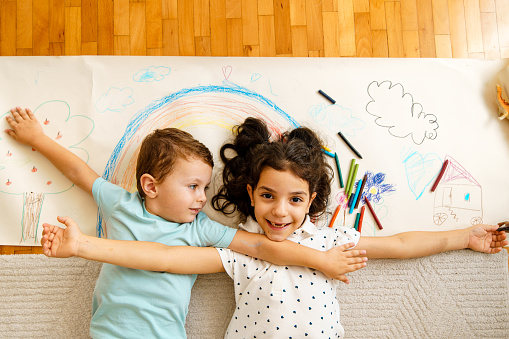 Above shot of two children embrace and posing with their crayon drawing on a paper roll
