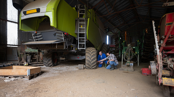 A young farmer apprentice being taught about the farming machinery  while working in a barn at the sustainable farm he works at in Embleton, North East England. The two men are looking at a combine harvester tyres.