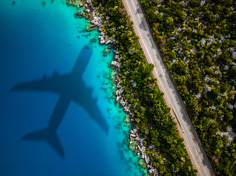 Vacation at tropical paradise near sea. Aerial view of beach and sea shore with airplane arriving at destination. Summer vacation background with place for text. Shoot directly above.