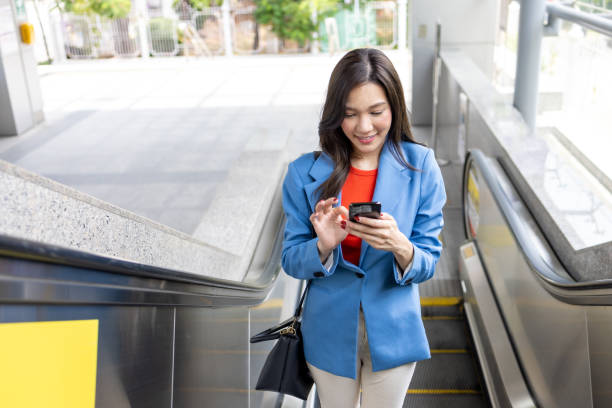 istock Asian woman using mobile phone while standing on escalator and going to office 1496087469