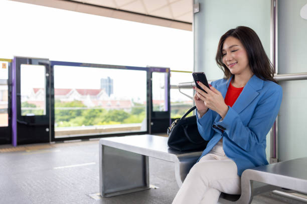 istock Asian woman using mobile phone while waiting for train to go to office 1496087489