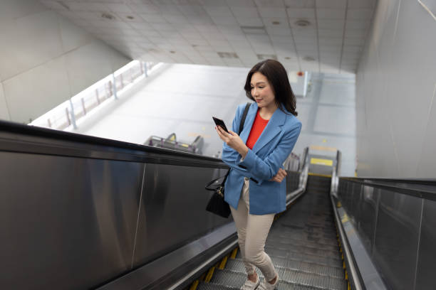 istock Asian woman using mobile phone while standing on escalator and going to office 1496087491