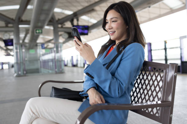 istock Asian woman using mobile phone while waiting for train to go to office 1496087520