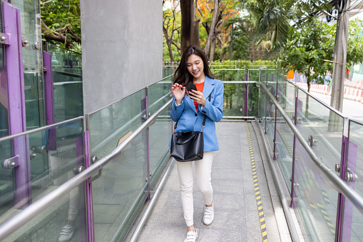 Asian woman using mobile phone while walking at skytrain on the way to office