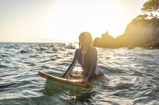 Woman in wetsuit with a surfboard on a sunny morning in the sea