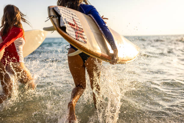 Rear view of surfers having fun while running into sea with surfboards at sunrise