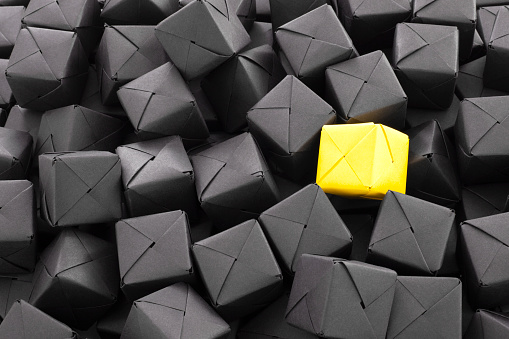 Close-up view of a yellow paper cube over lots of black ones for identity concept