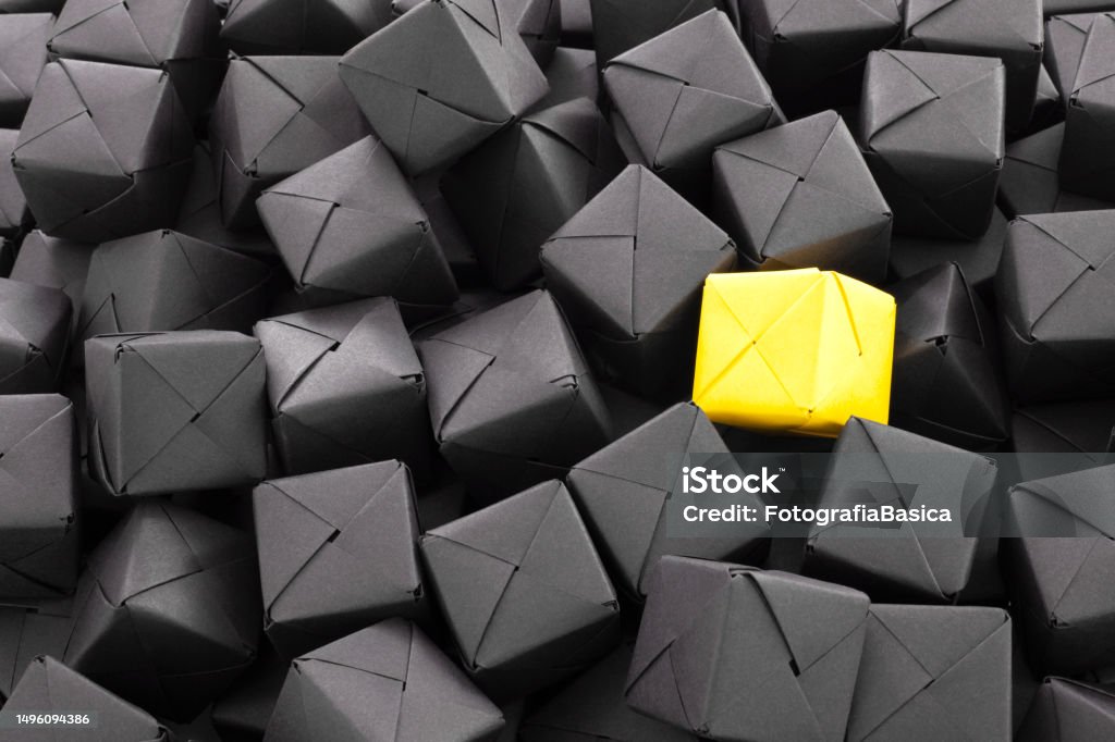 Lonely yellow cube Close-up view of a yellow paper cube over lots of black ones for identity concept Repetition Stock Photo