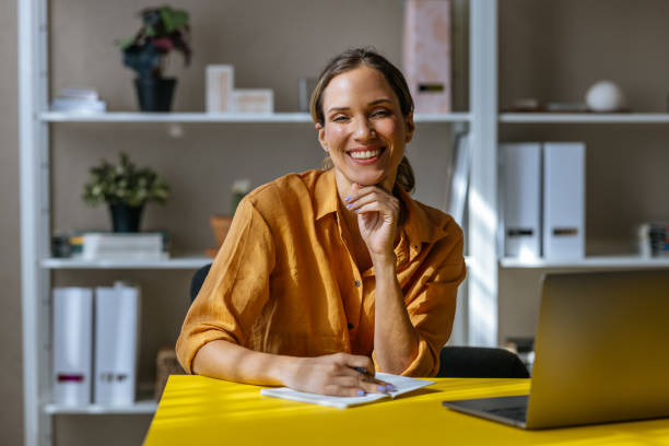 istock A Happy Beautiful Blonde Businesswoman Looking At Camera While Taking Some Notes In Her Notebook 1496098121