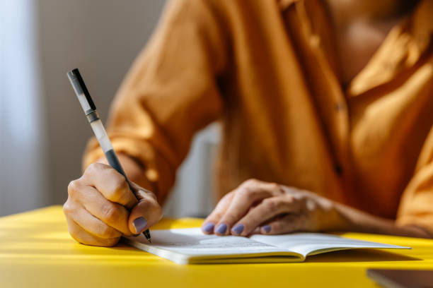 an unrecognizable businesswoman taking some notes in her notebook while working in the office - writing instrument imagens e fotografias de stock