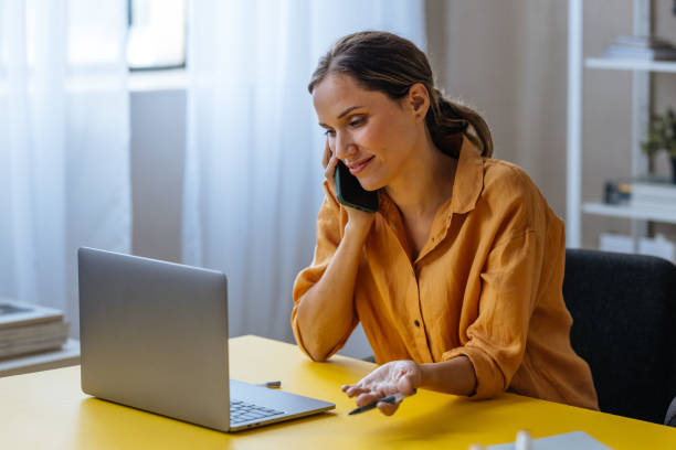 istock A Happy Beautiful Blonde Businesswoman Using Her Mobile Phone While Working On Her Computer 1496098137