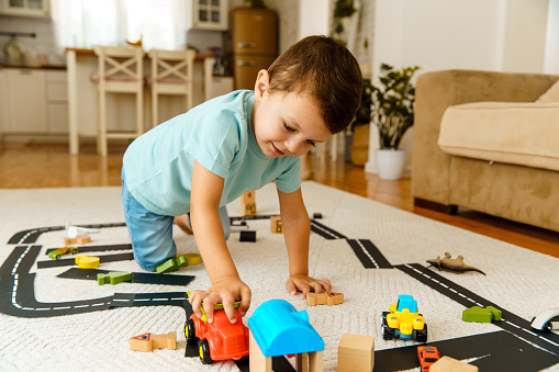 Top view of boy playing with colorful plastic bricks at the white table. Developing toys: car and bus from plastic bricks