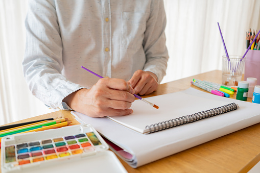 Man asian sitting and painting watercolour artwork to develop abilities and improve mental health at home. Female artist drawing with inspiration.