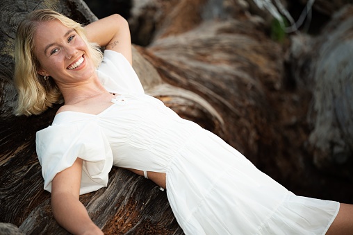 A young, attractive Caucasian blonde female smiling and posing in a white dress